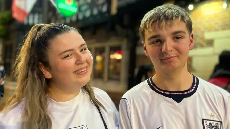A woman and a man standing side-by-side in England shirts.